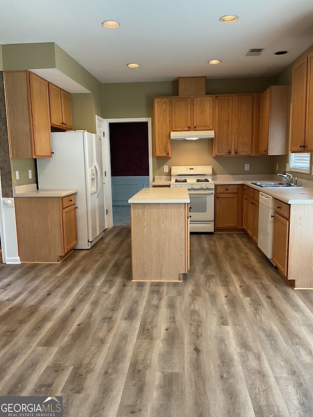 kitchen with white appliances, under cabinet range hood, a sink, and wood finished floors