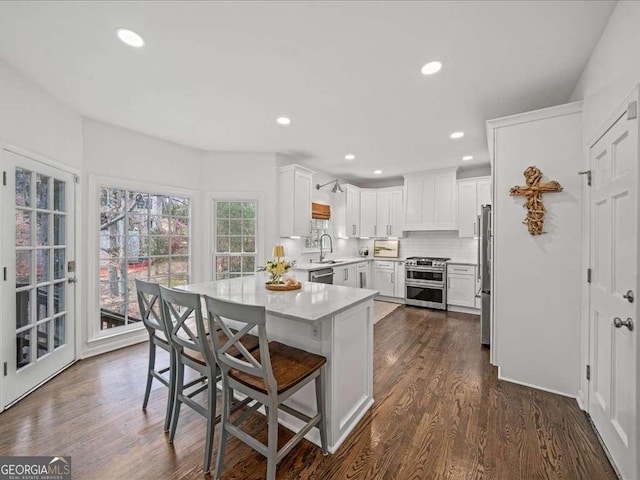 kitchen featuring a breakfast bar area, stainless steel appliances, dark wood-type flooring, a sink, and light countertops