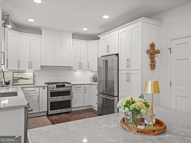 kitchen with stainless steel appliances, white cabinetry, light stone counters, and tasteful backsplash