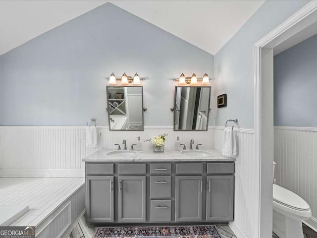 bathroom with a wainscoted wall, a sink, toilet, and lofted ceiling