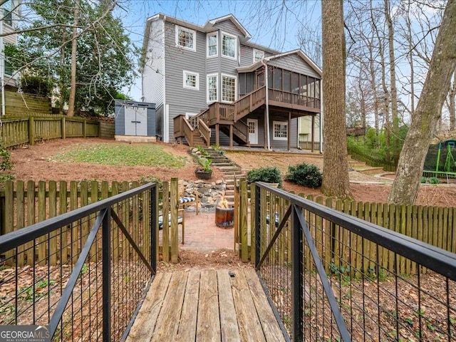 back of house with a sunroom, a fenced backyard, an outbuilding, stairs, and a shed