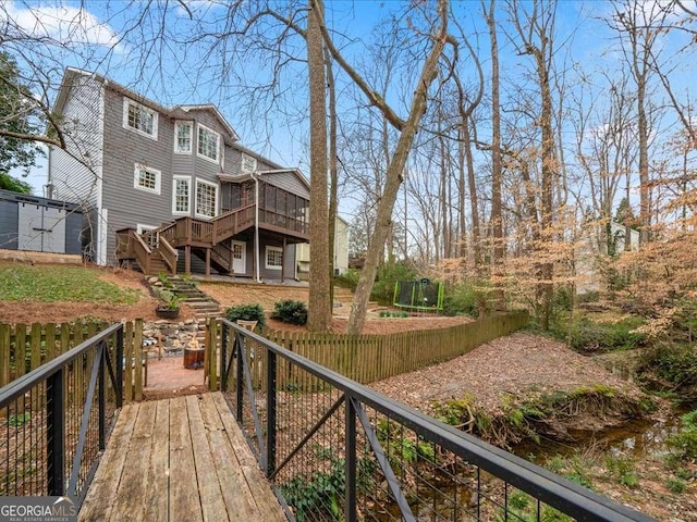 back of property with a trampoline, a deck, and stairs