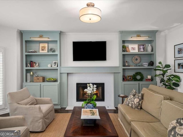 living room with a lit fireplace, built in shelves, crown molding, and wood finished floors