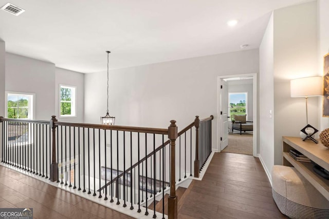 hall with baseboards, visible vents, an upstairs landing, and wood finished floors