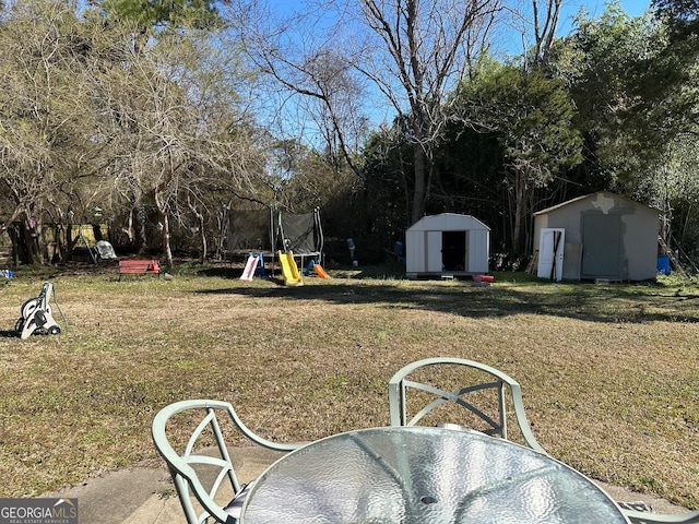 view of yard featuring an outbuilding, a storage unit, a trampoline, and outdoor dining space