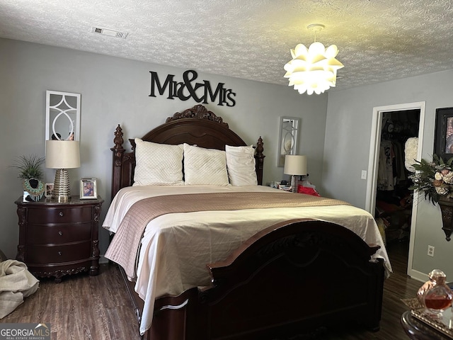 bedroom featuring a notable chandelier, a textured ceiling, visible vents, and wood finished floors