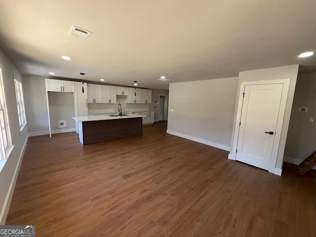 unfurnished living room with dark wood-style floors, visible vents, baseboards, and a sink