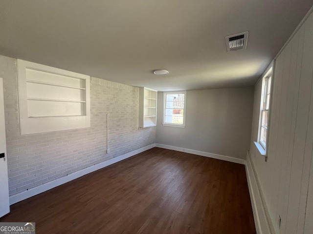 empty room featuring visible vents, built in shelves, brick wall, baseboards, and dark wood-style flooring