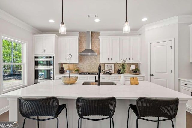 kitchen with a sink, visible vents, ornamental molding, appliances with stainless steel finishes, and wall chimney exhaust hood