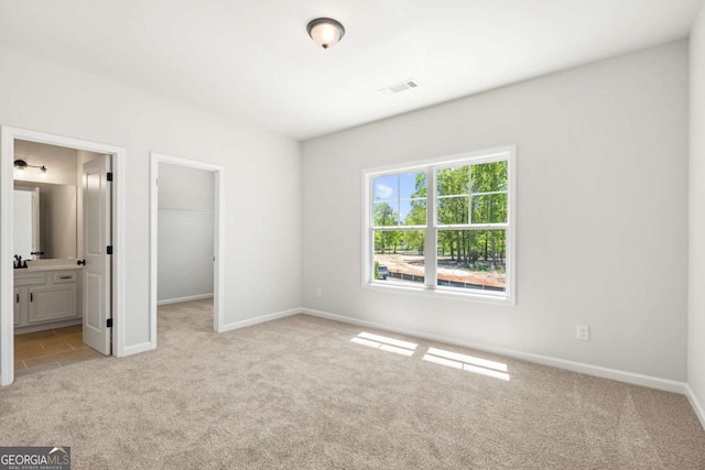 unfurnished bedroom with connected bathroom, light colored carpet, visible vents, baseboards, and a walk in closet