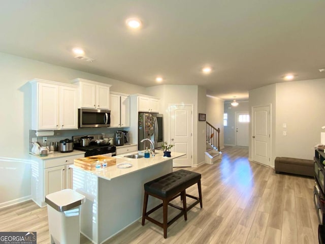 kitchen with a center island with sink, white cabinets, stainless steel appliances, light wood-style floors, and a sink