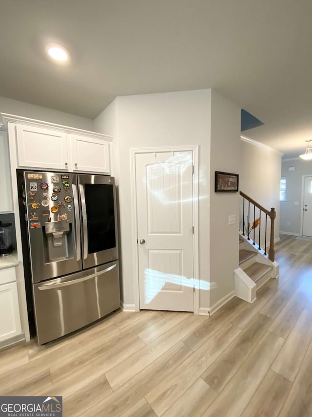 kitchen with stainless steel fridge, light wood-style flooring, baseboards, and white cabinetry