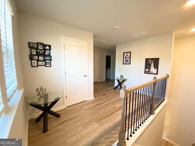 hallway with light wood-style flooring, plenty of natural light, an upstairs landing, and baseboards