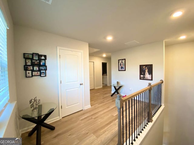 hallway featuring baseboards, light wood-style flooring, an upstairs landing, and recessed lighting