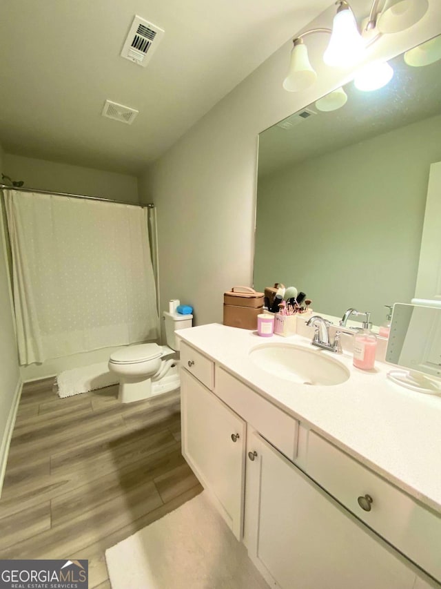 bathroom with toilet, vanity, wood finished floors, and visible vents