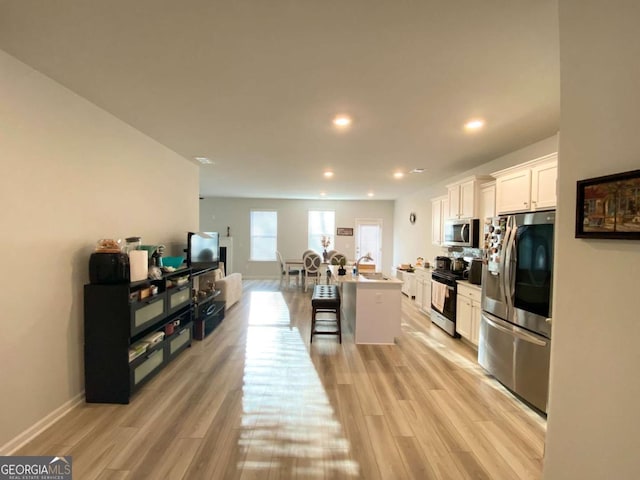 kitchen with white cabinets, light wood finished floors, a kitchen bar, and stainless steel appliances