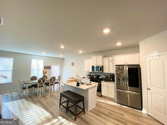 kitchen featuring stainless steel appliances, white cabinets, light wood-style flooring, and a breakfast bar area