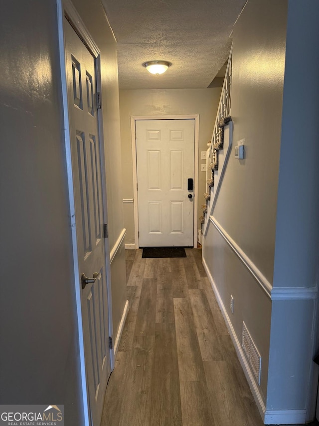 doorway featuring stairway, visible vents, dark wood finished floors, and a textured ceiling