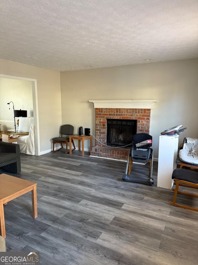 living area featuring a brick fireplace, a textured ceiling, baseboards, and wood finished floors