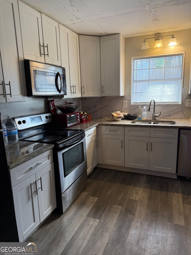 kitchen with dark wood-style flooring, light stone countertops, stainless steel appliances, white cabinetry, and a sink