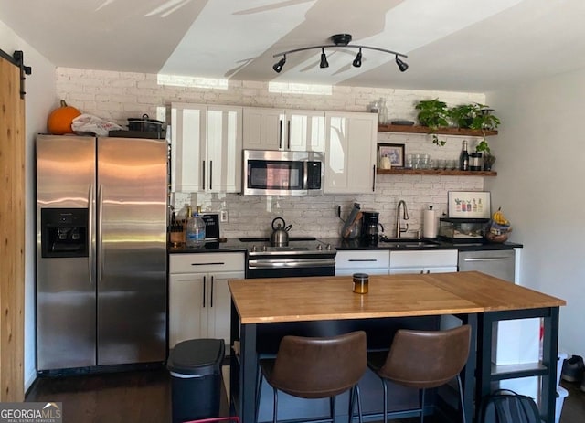 kitchen with tasteful backsplash, a barn door, white cabinets, appliances with stainless steel finishes, and a sink