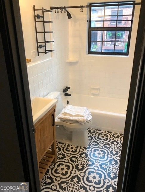 full bathroom featuring shower / tub combination, toilet, tile patterned flooring, vanity, and tile walls