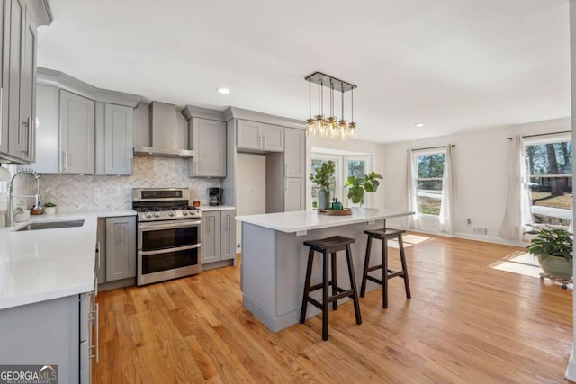 kitchen featuring range with two ovens, wall chimney range hood, gray cabinets, and a sink