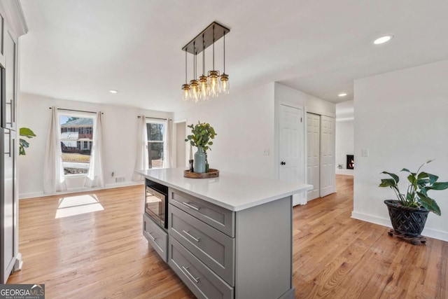 kitchen featuring decorative light fixtures, gray cabinets, light countertops, stainless steel microwave, and light wood-style floors