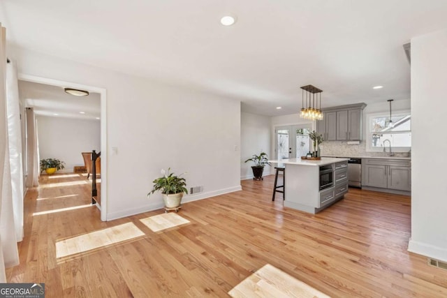 kitchen with light countertops, light wood-style flooring, stainless steel dishwasher, gray cabinetry, and a kitchen breakfast bar