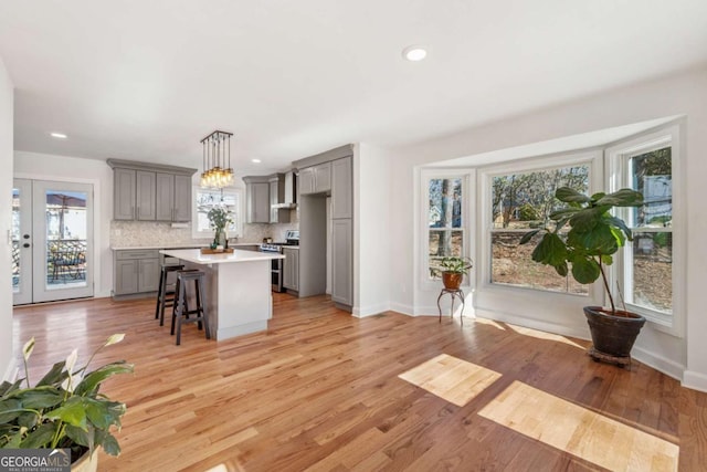 kitchen featuring gray cabinets, light countertops, light wood-type flooring, double oven range, and backsplash