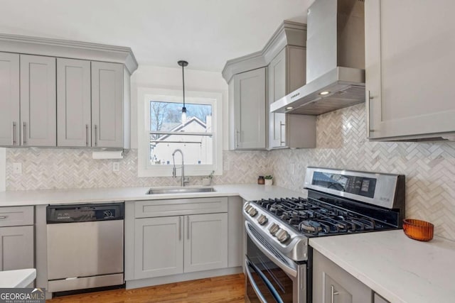 kitchen with stainless steel appliances, gray cabinets, a sink, and wall chimney range hood