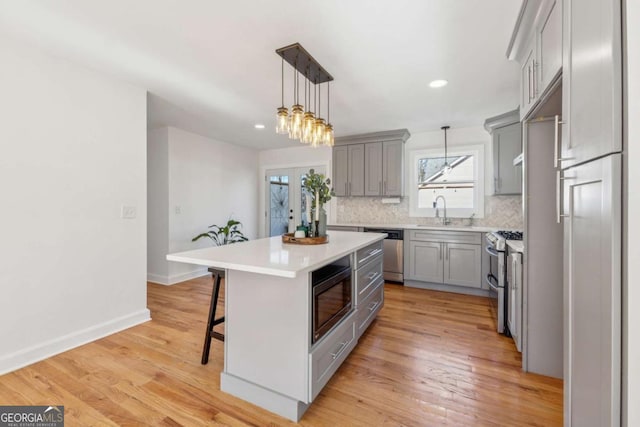 kitchen with stainless steel appliances, gray cabinets, a sink, and backsplash