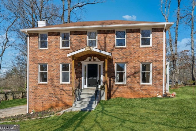 colonial-style house with brick siding, a chimney, and a front lawn