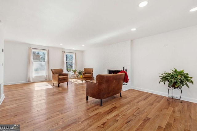 living area with light wood-type flooring, a brick fireplace, baseboards, and recessed lighting