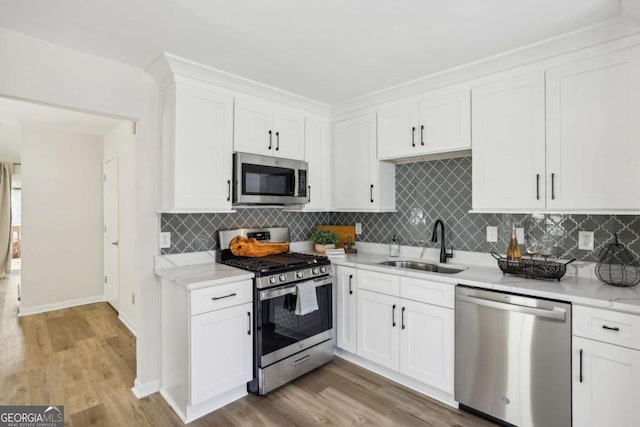 kitchen with white cabinets, light wood finished floors, stainless steel appliances, and a sink