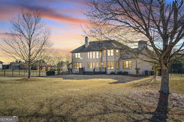 rear view of property featuring a chimney, fence, central AC, and a yard