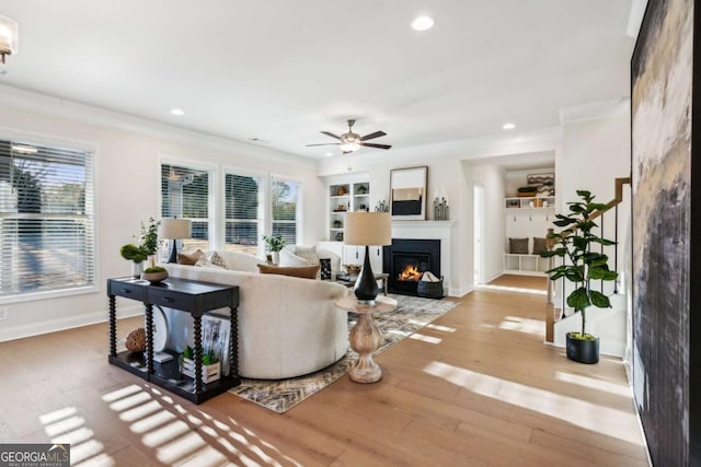 living room featuring baseboards, built in shelves, wood finished floors, and crown molding