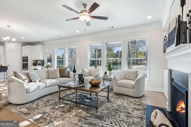 living area featuring visible vents, wood finished floors, a lit fireplace, baseboards, and ceiling fan with notable chandelier