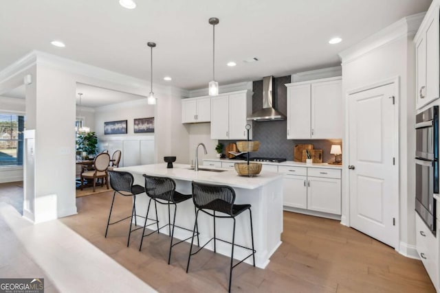 kitchen with wall chimney exhaust hood, crown molding, white cabinets, and a sink