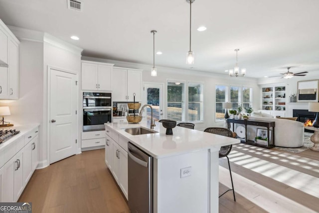 kitchen with stainless steel appliances, a sink, white cabinets, a kitchen bar, and a glass covered fireplace