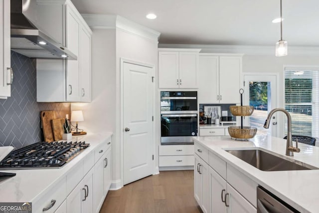 kitchen featuring a sink, white cabinetry, light countertops, appliances with stainless steel finishes, and wall chimney exhaust hood