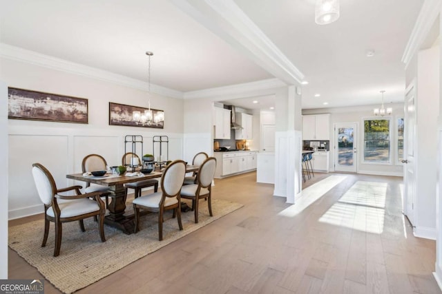 dining area featuring a chandelier, light wood finished floors, crown molding, and a decorative wall