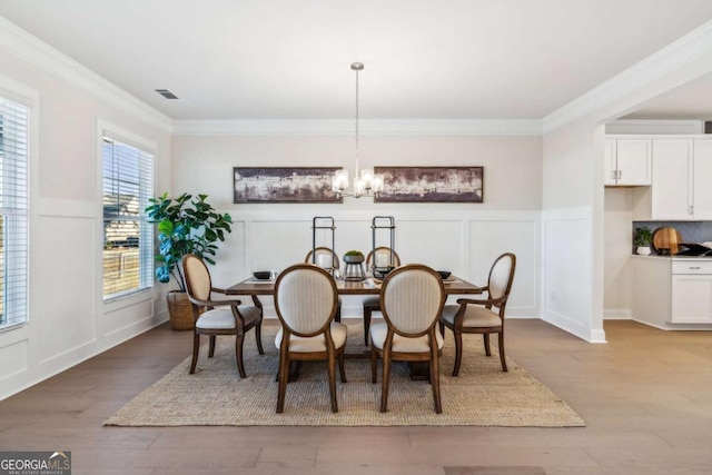 dining space featuring a notable chandelier, ornamental molding, wood finished floors, and a decorative wall