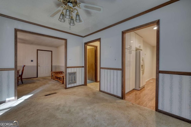 unfurnished room with light colored carpet, visible vents, ornamental molding, a ceiling fan, and wainscoting