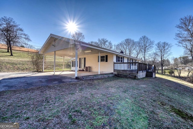 exterior space featuring driveway, a deck, a carport, and a yard