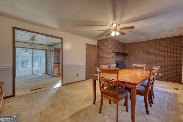 dining area with a textured ceiling, ceiling fan, light carpet, brick wall, and visible vents