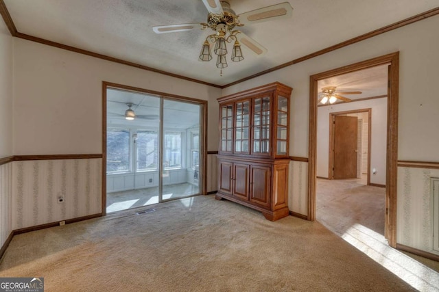 unfurnished dining area with wainscoting, light colored carpet, crown molding, and visible vents