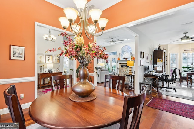 dining room with wood finished floors, a fireplace, baseboards, and ceiling fan with notable chandelier