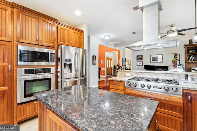 kitchen with brown cabinets, island exhaust hood, stainless steel appliances, a ceiling fan, and open floor plan