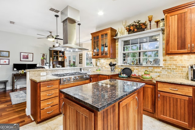 kitchen featuring island range hood, stainless steel gas cooktop, a peninsula, visible vents, and backsplash